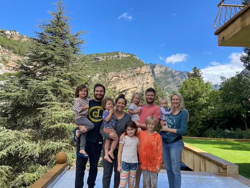 Group stands together on outdoor deck with scenic mountain landscape and evergreen trees in background.