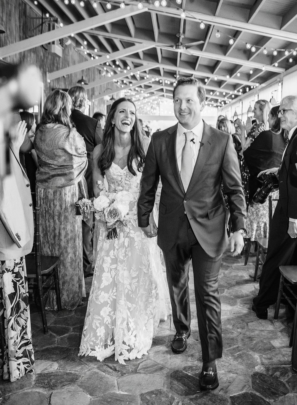 A joyful wedding celebration in a rustic covered venue with stone flooring and wooden beams overhead.