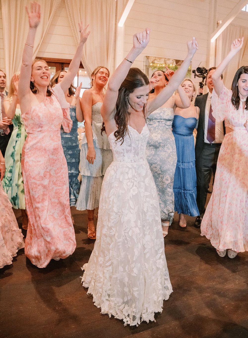 Wedding celebration with dancing guests in formal attire raising their hands during a reception in an elegant venue.