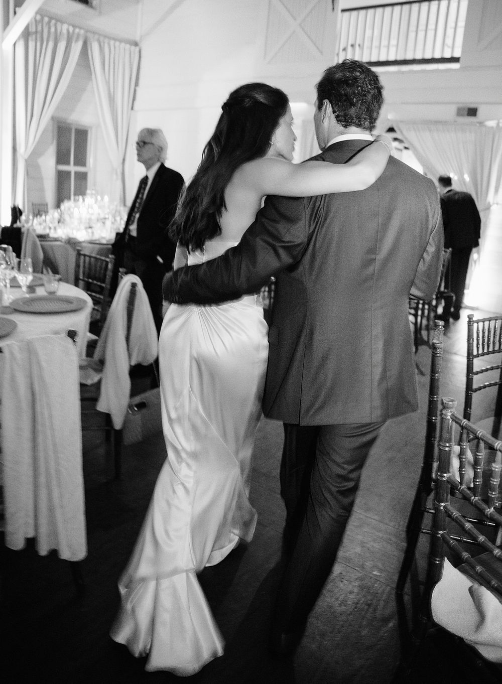 A couple embraces while dancing at an elegant wedding reception in a white-draped ballroom.