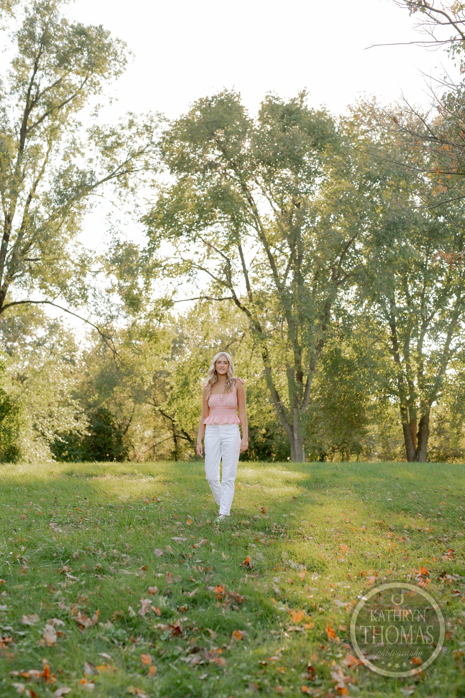 A full-length portrait against tall trees with scattered autumn leaves on the ground.