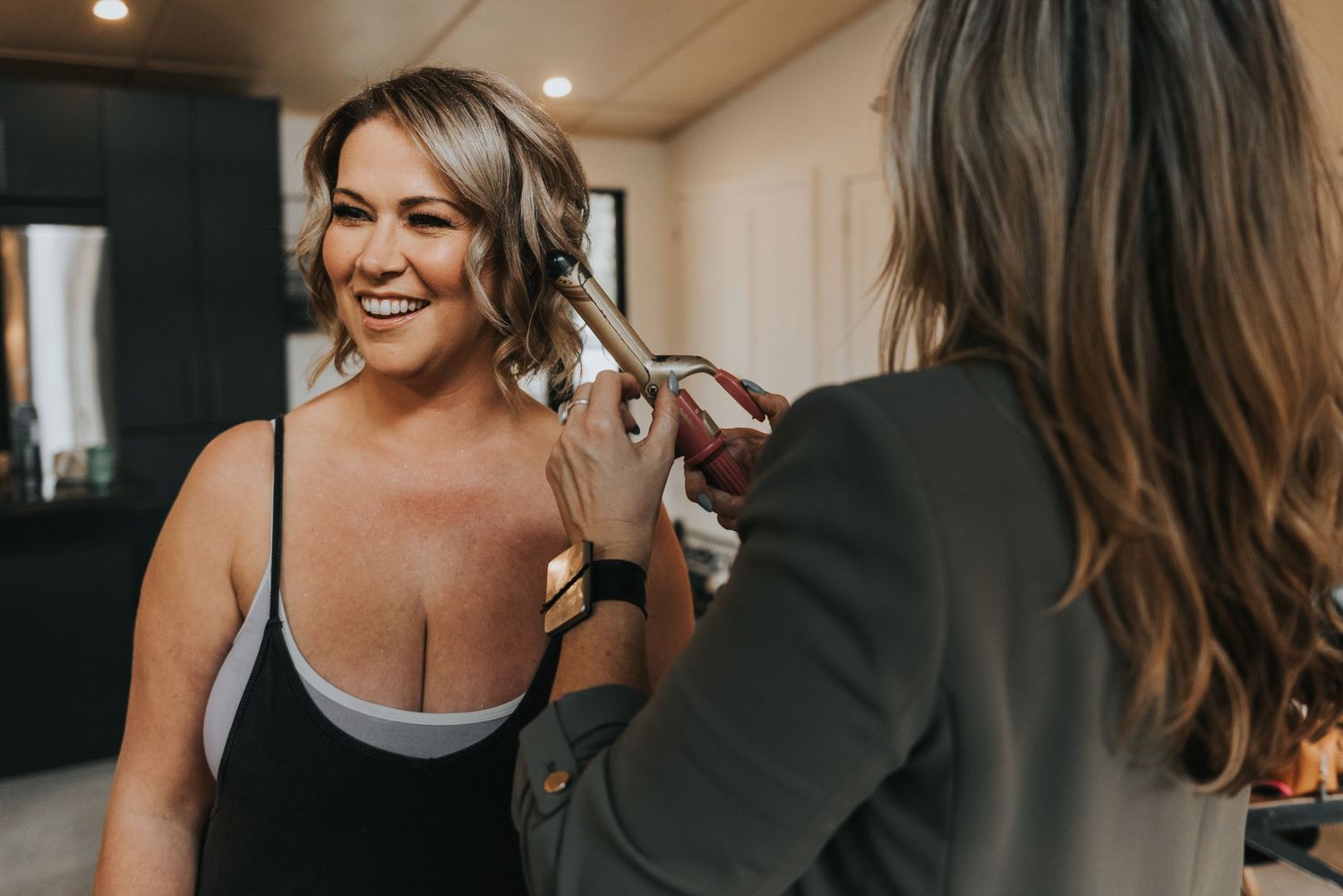 Hair stylist using a curling iron to style client's hair in a warmly lit salon interior.