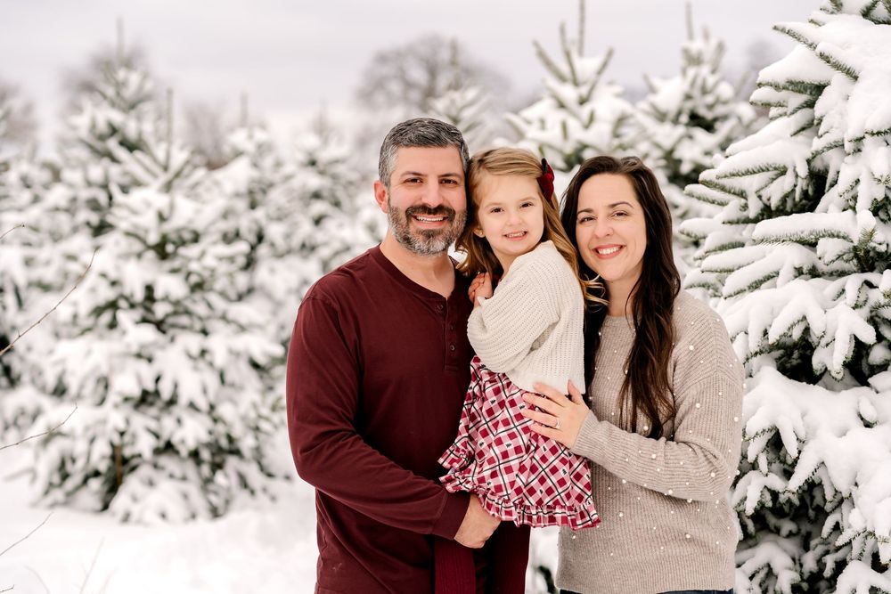 A family poses together among snow-covered evergreen trees in a winter wonderland setting.
