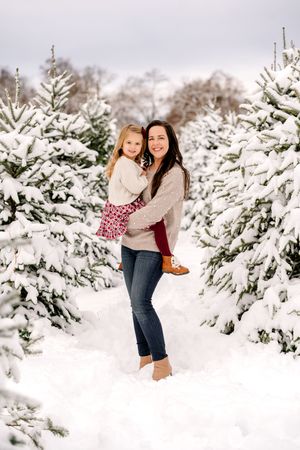 Two people laugh and play together in a snowy winter scene among snow-covered evergreen trees.