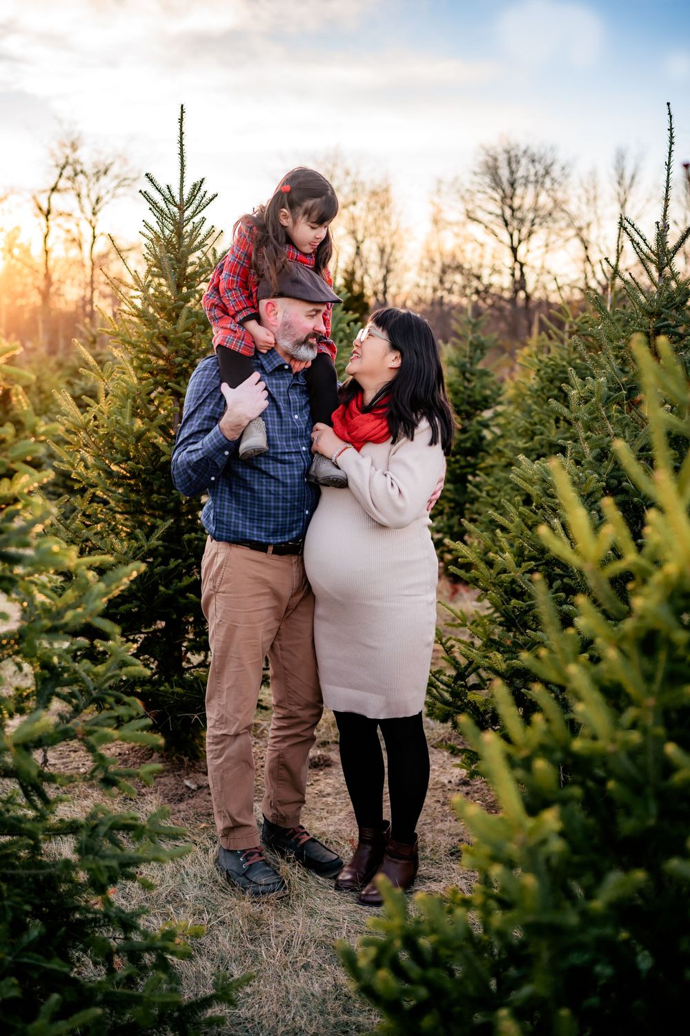 A family shares a tender moment together at a Christmas tree farm during sunset.