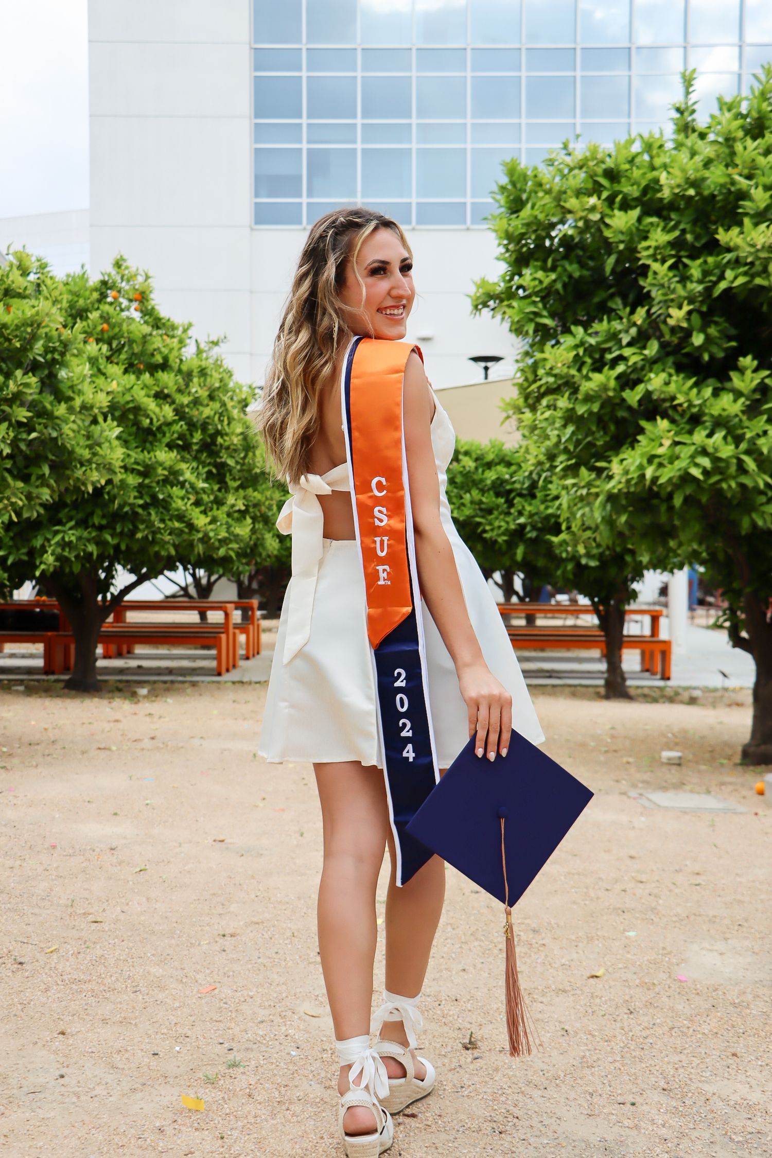 Graduate poses with decorated graduation cap featuring navy and orange design.