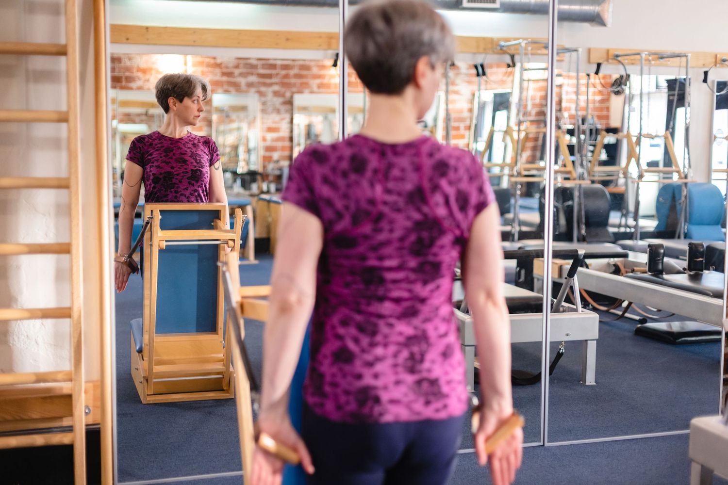 Person wearing purple velvet top exercises while looking in gym mirror with fitness equipment in background.