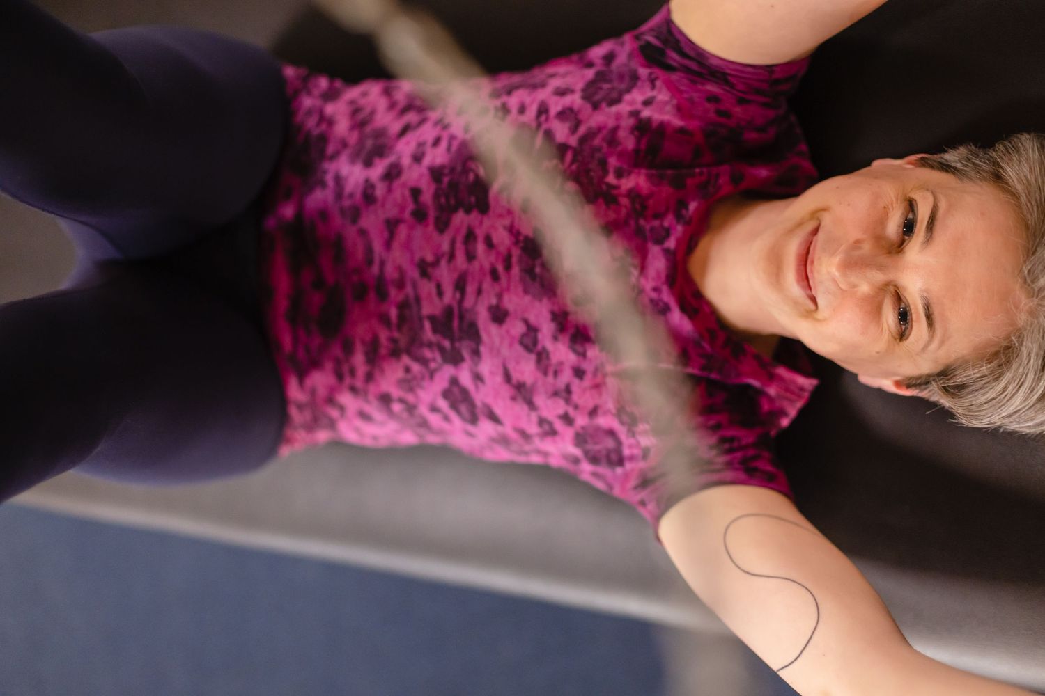 Person wearing bright pink velvet top lies on floor during workout session at fitness studio.