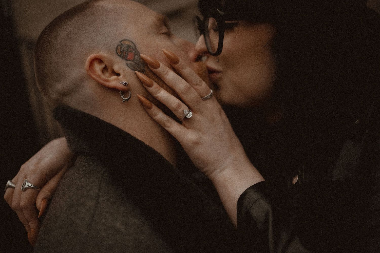 An intimate moment between a couple in dark moody lighting as a hand with silver rings reaches towards a face.