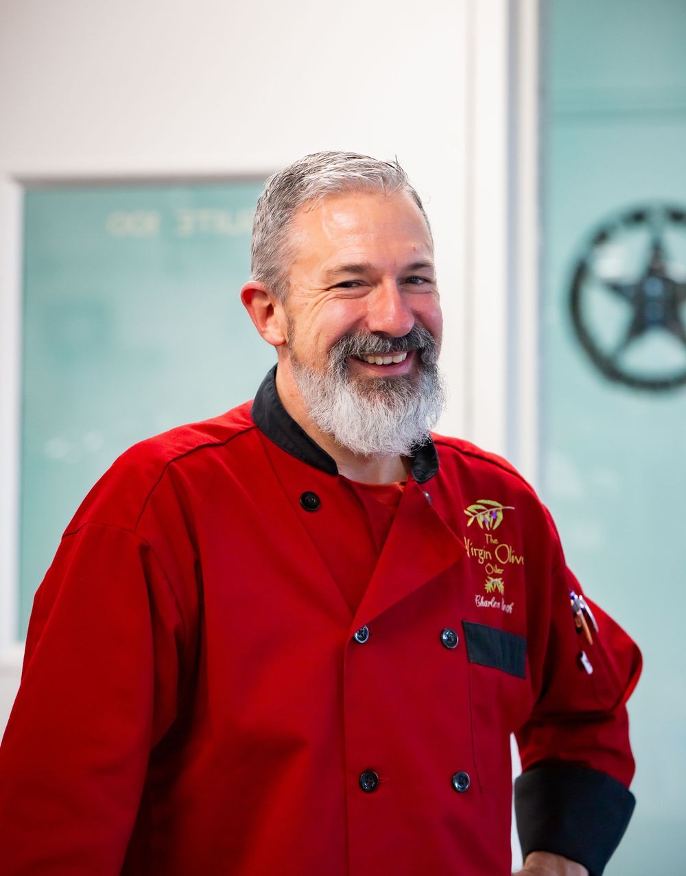 A chef in a red uniform smiling warmly in a commercial kitchen setting.