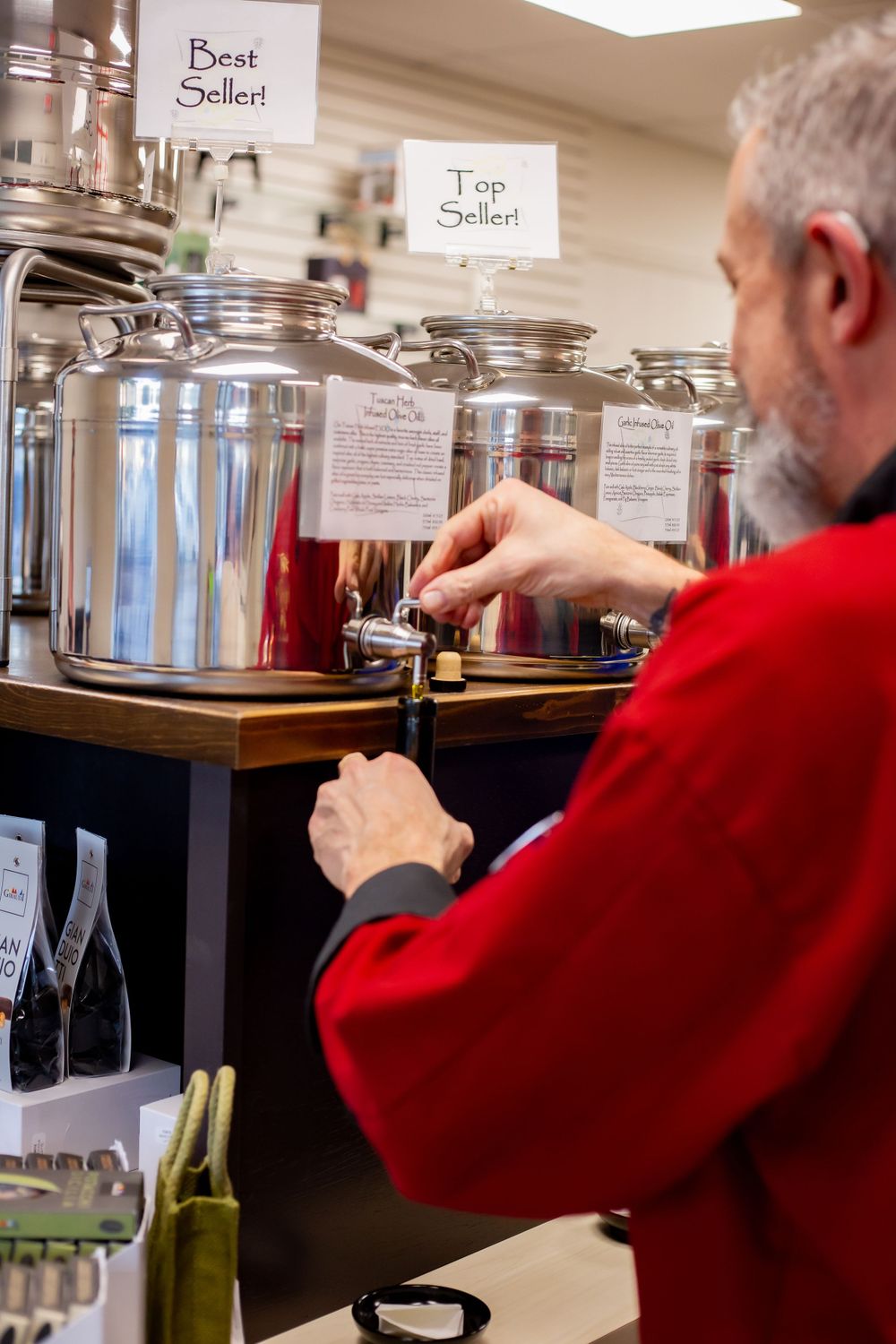 Person in red chef coat pouring olive oil from stainless steel containers.