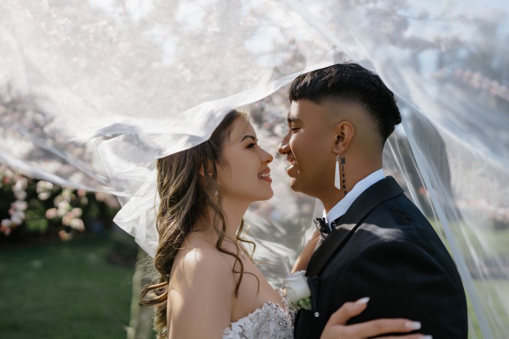 Two people share an intimate moment outdoors, with soft light and a white veil blowing in the breeze.