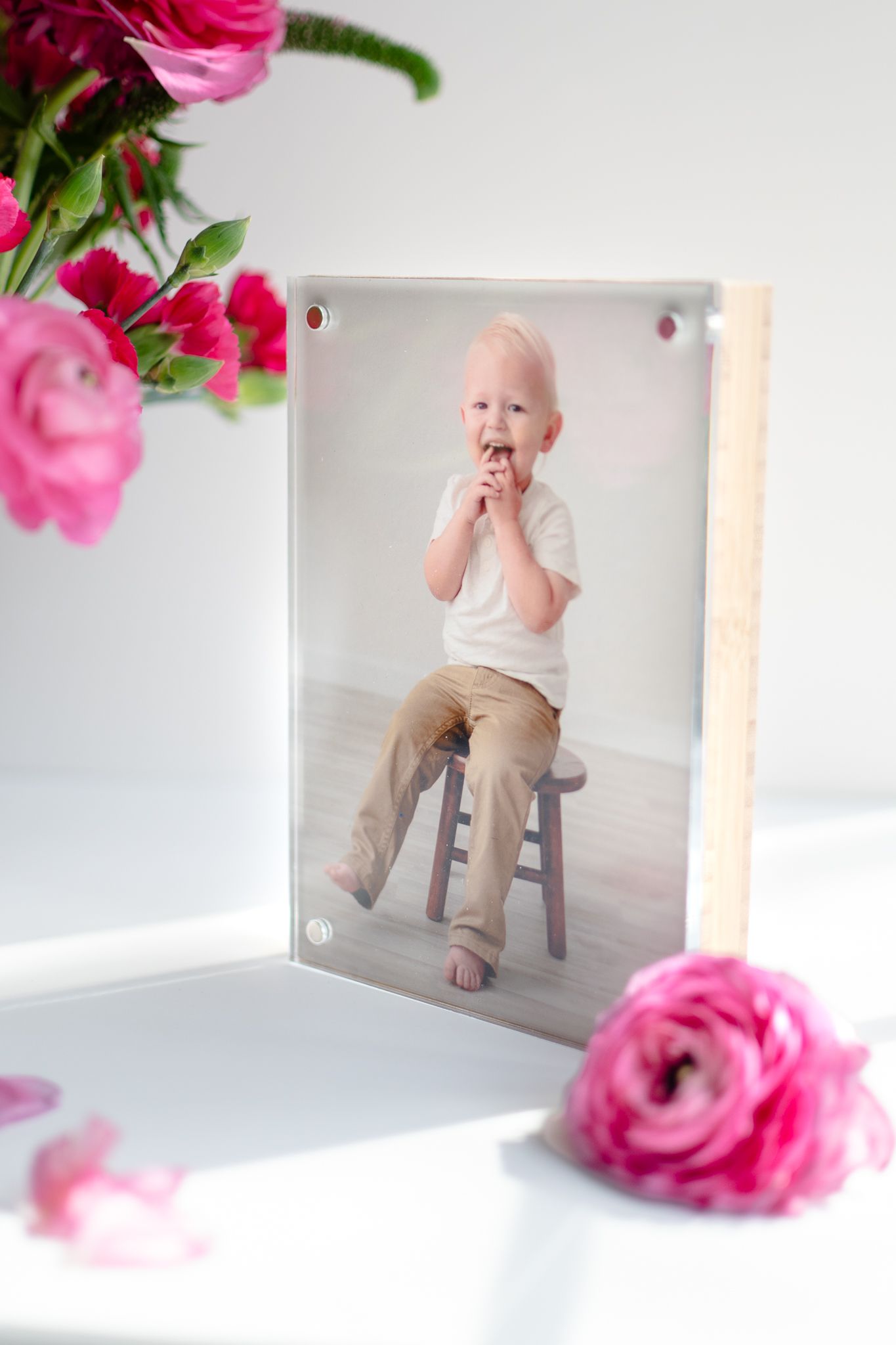 A framed photo displayed on white surface with pink floral decorations including roses and carnations.
