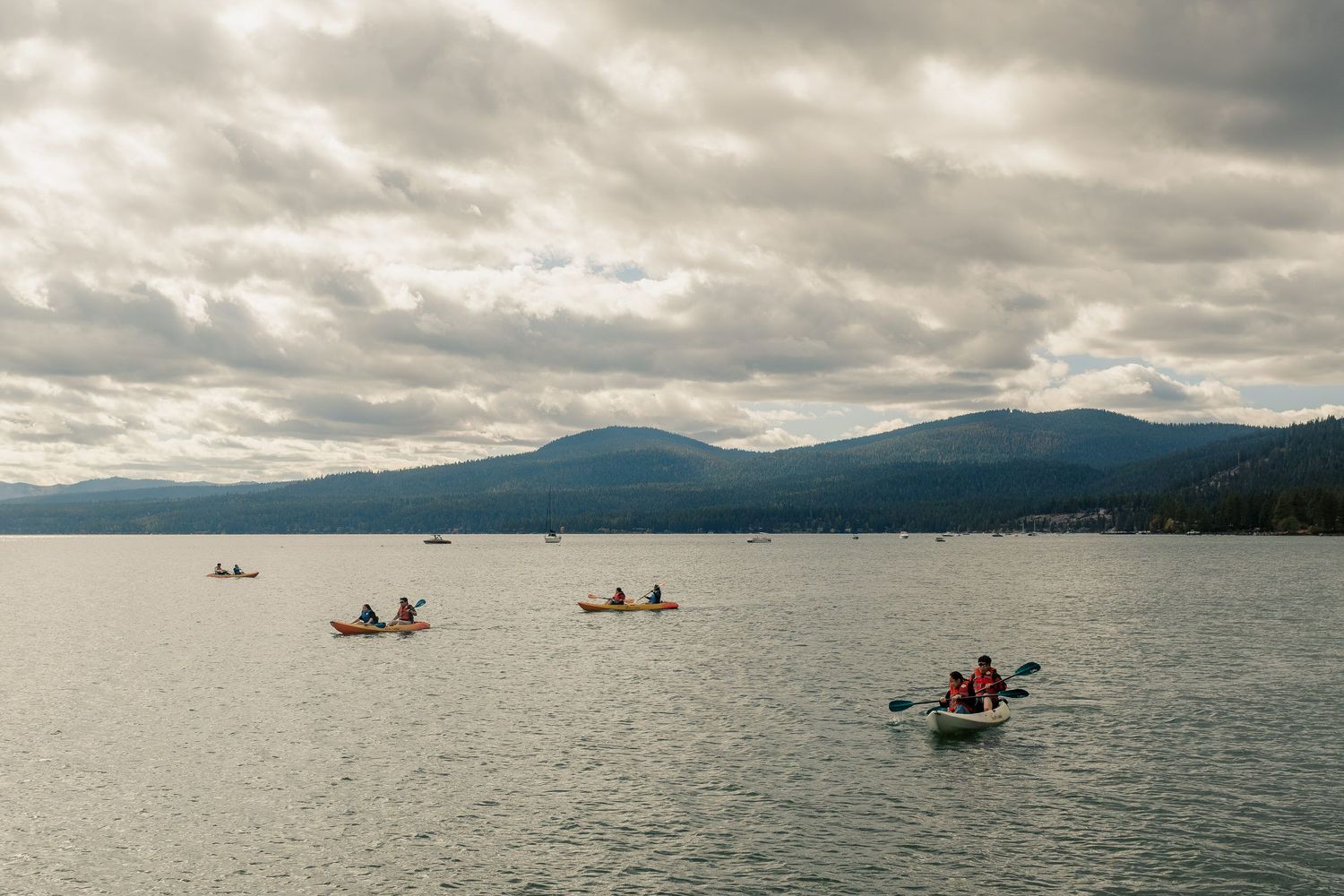 Kayakers paddle in Lake Tahoe surrounded by mountains under dramatic cloudy skies.