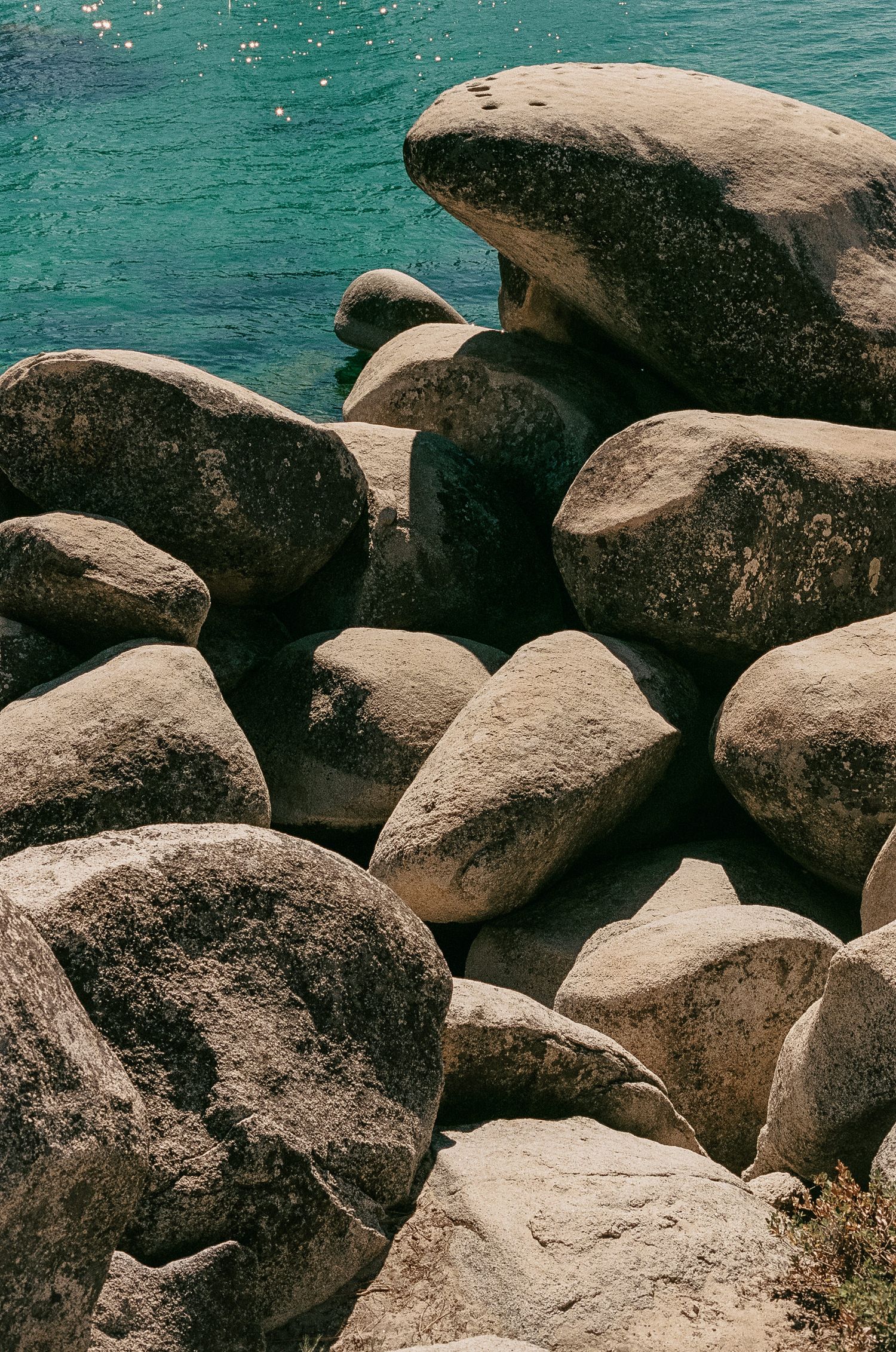 Large smooth granite boulders stacked along turquoise water at Lake Tahoe create a natural rocky shoreline.