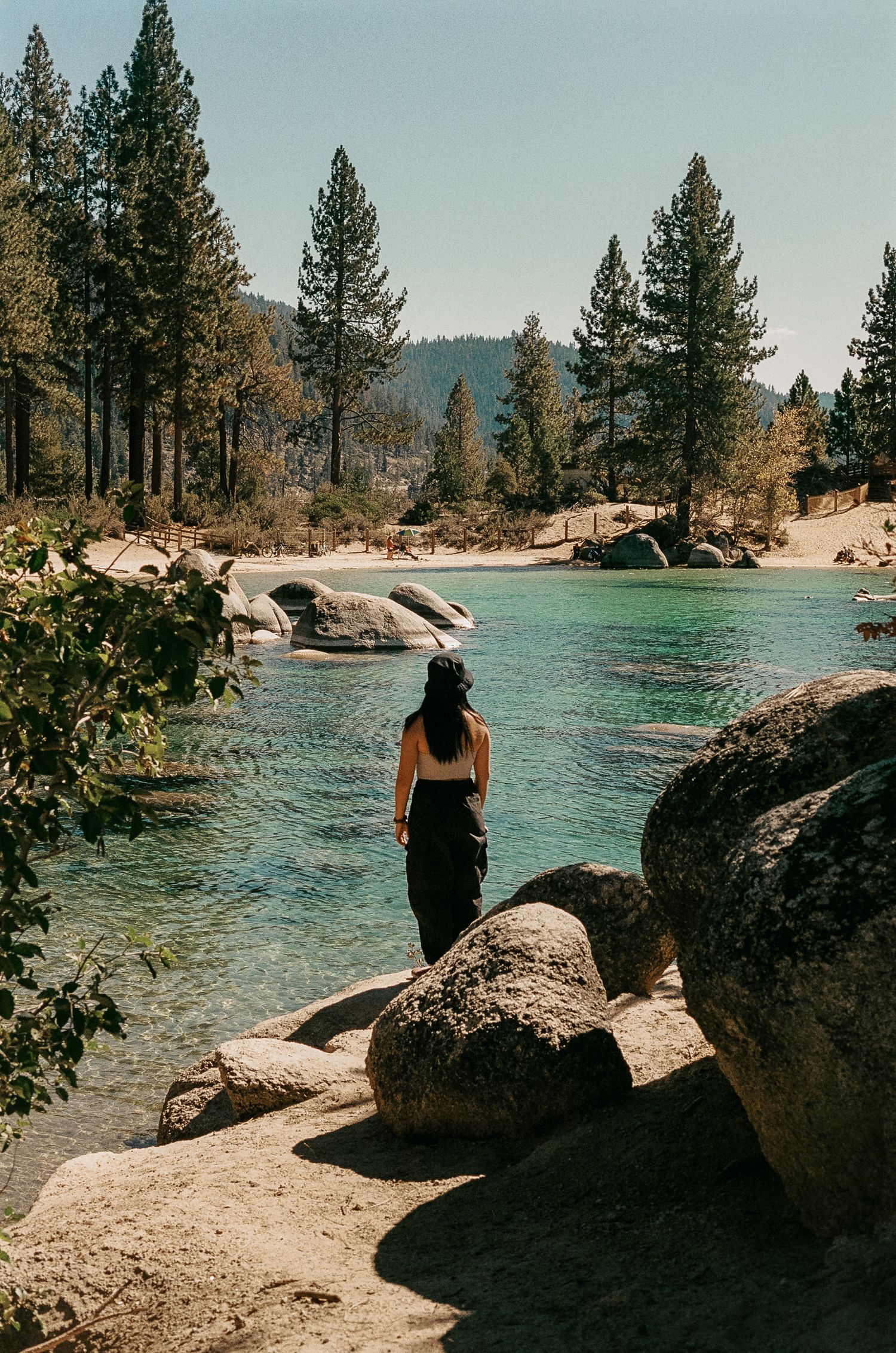 A tranquil turquoise lake surrounded by pine trees and large boulders in a serene mountain setting.