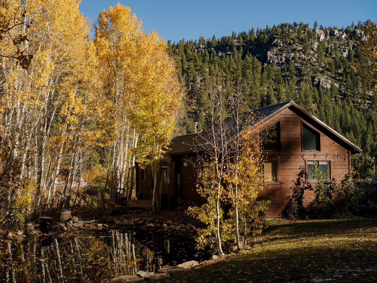 A rustic log cabin nestled among golden aspen trees during fall in a mountainous forest setting.