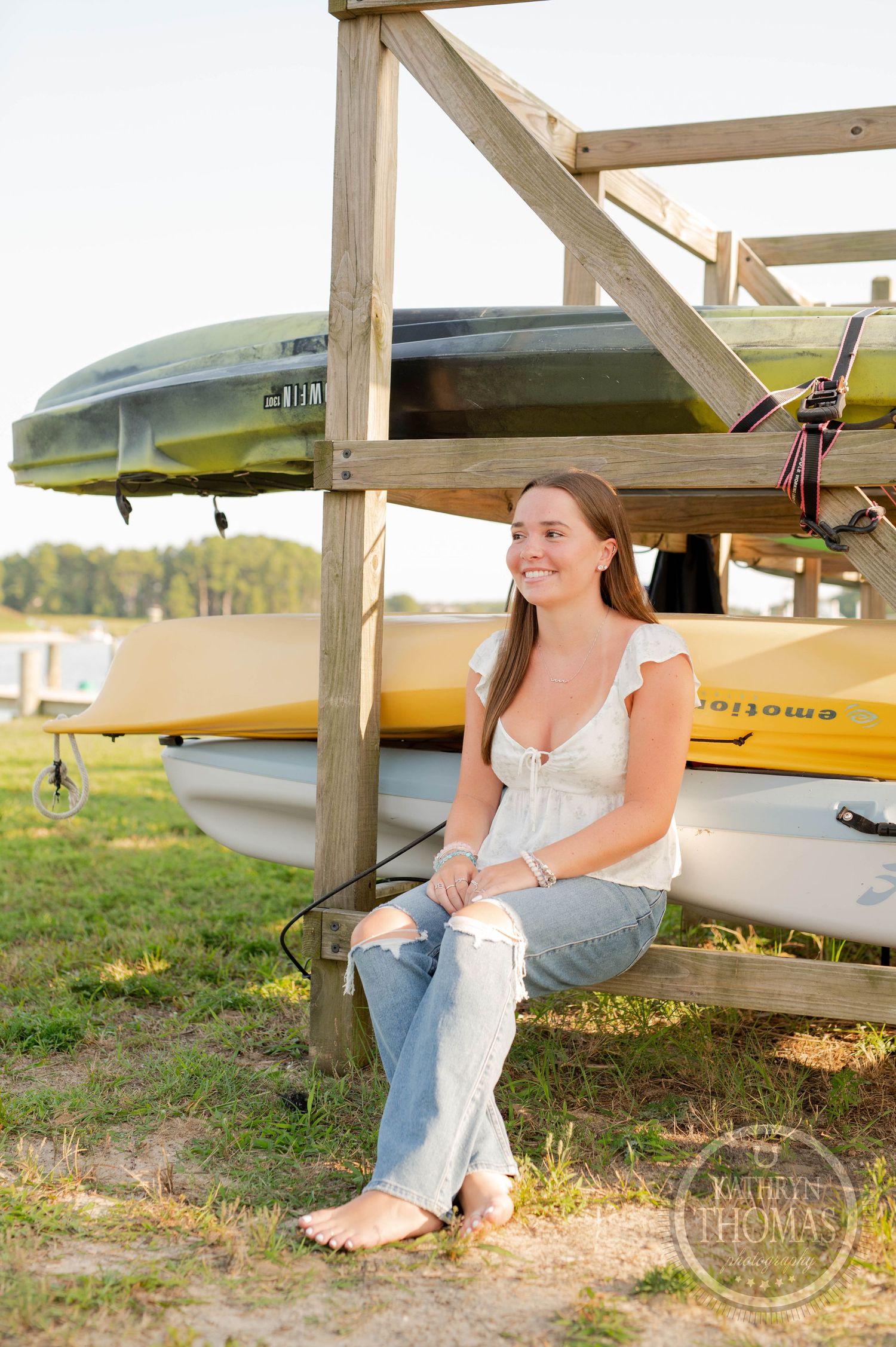 Someone sitting casually on a wooden kayak storage rack with boats in the background.
