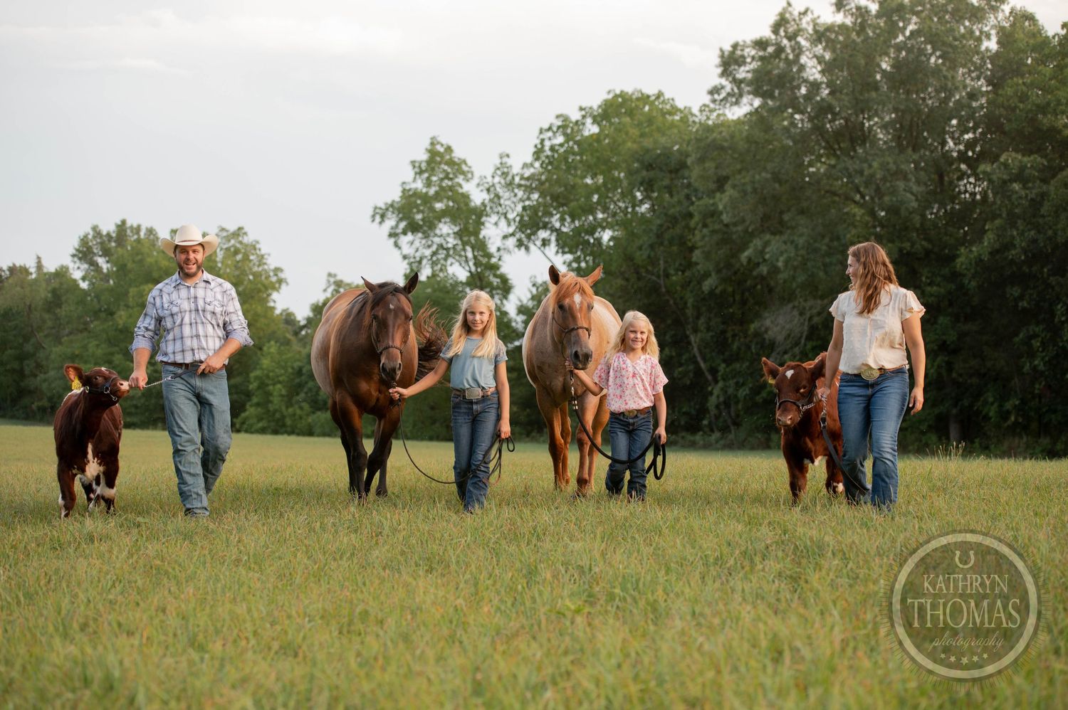 A group walks their horses and calves across a sunlit meadow.