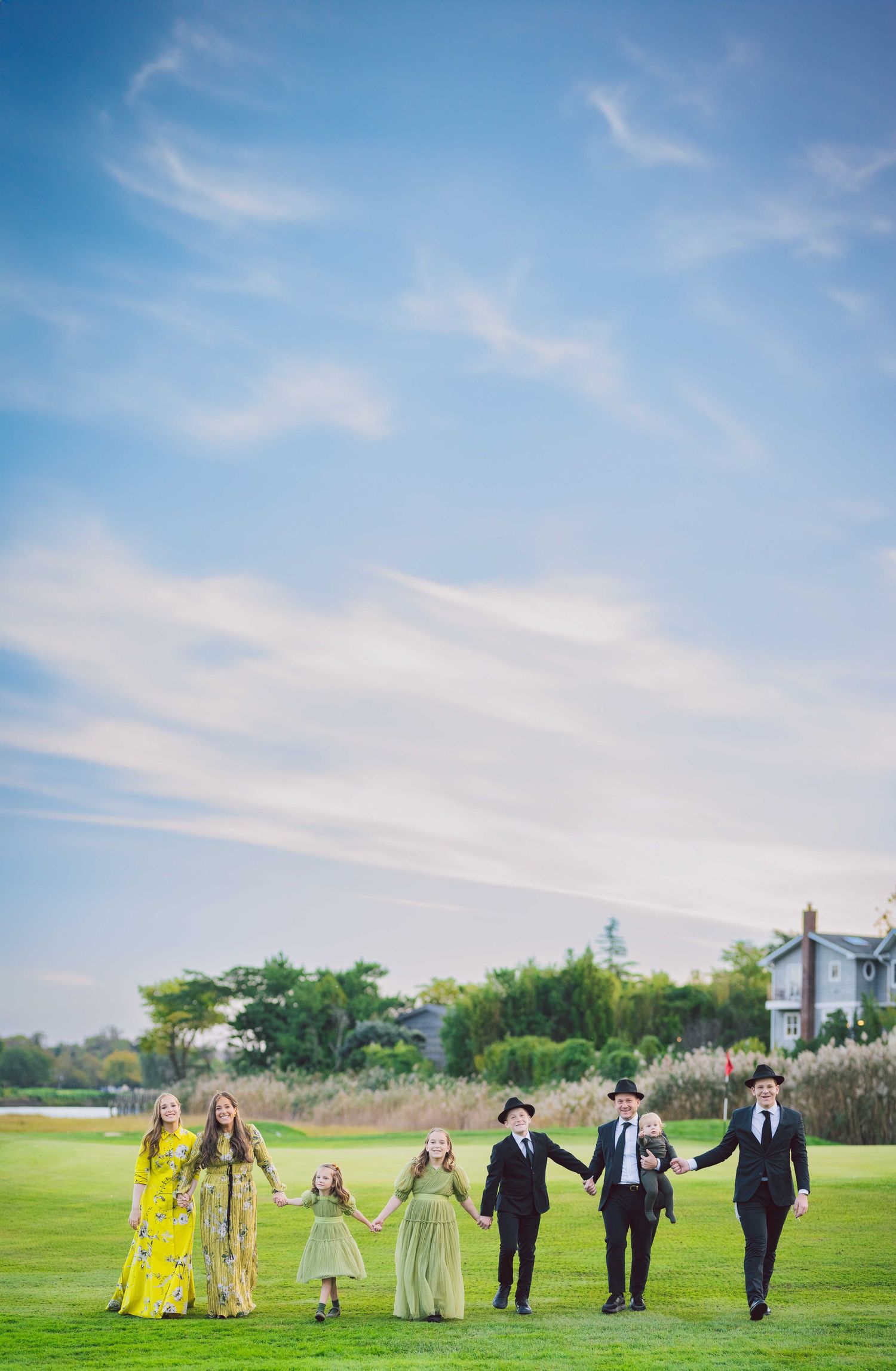 Wedding party walking across a green field under blue skies wearing yellow and formal attire.