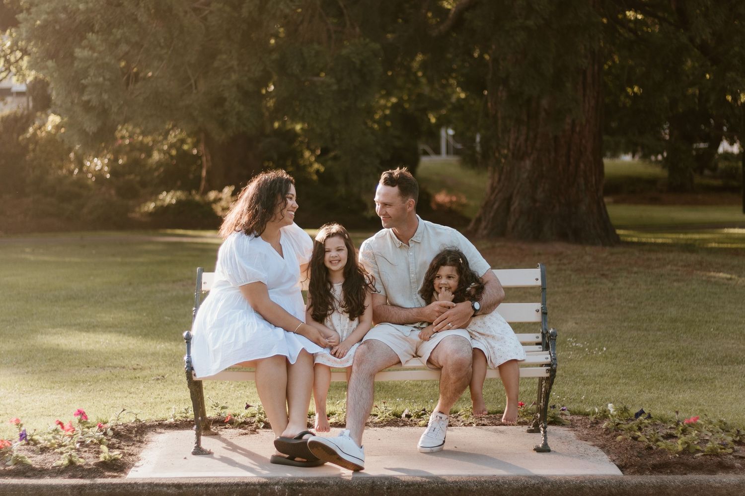 Family of 4 sitting on a park bench smiling at each other