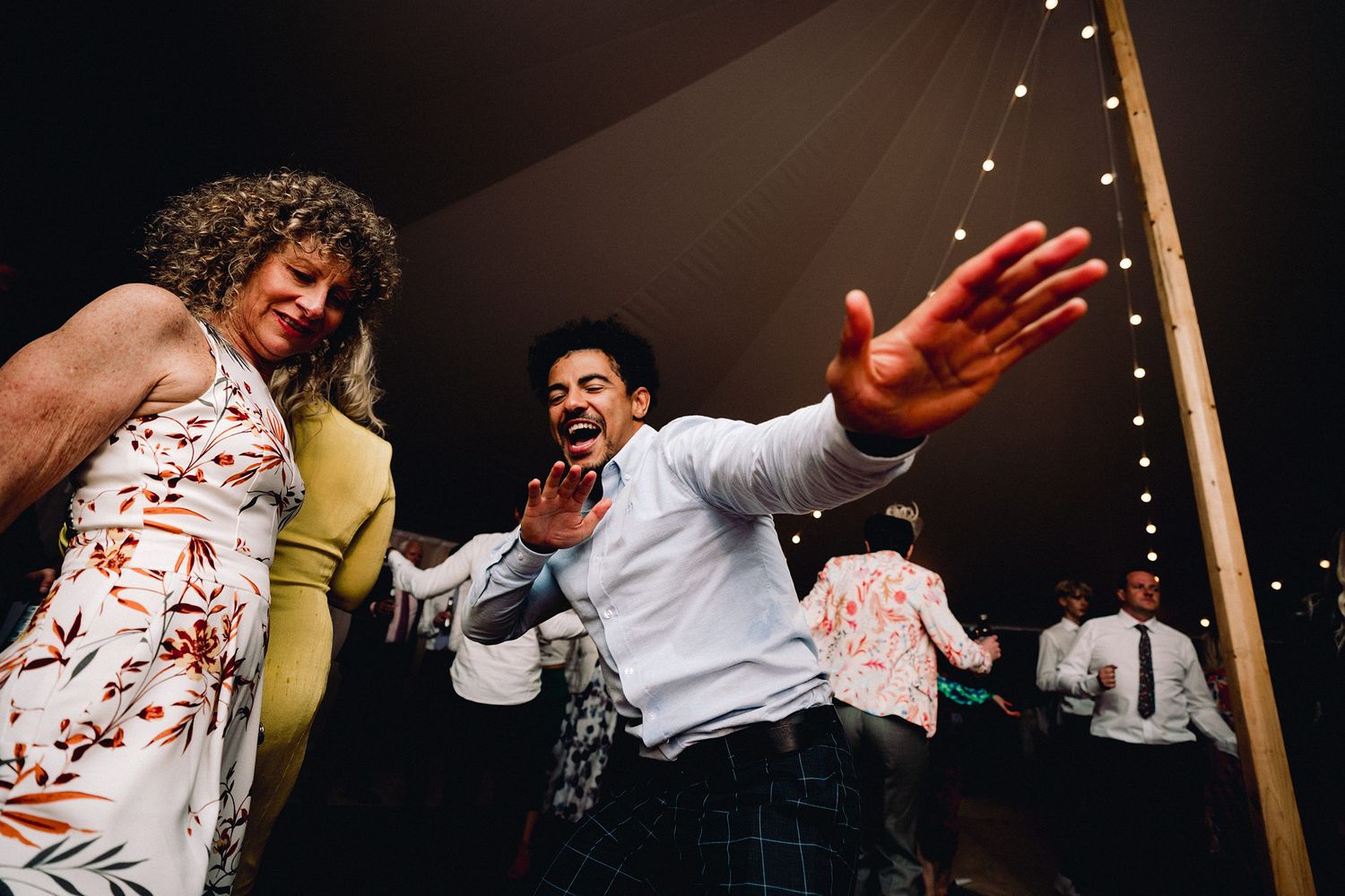 People dancing and celebrating together at a lively party under decorative lights in an indoor setting.