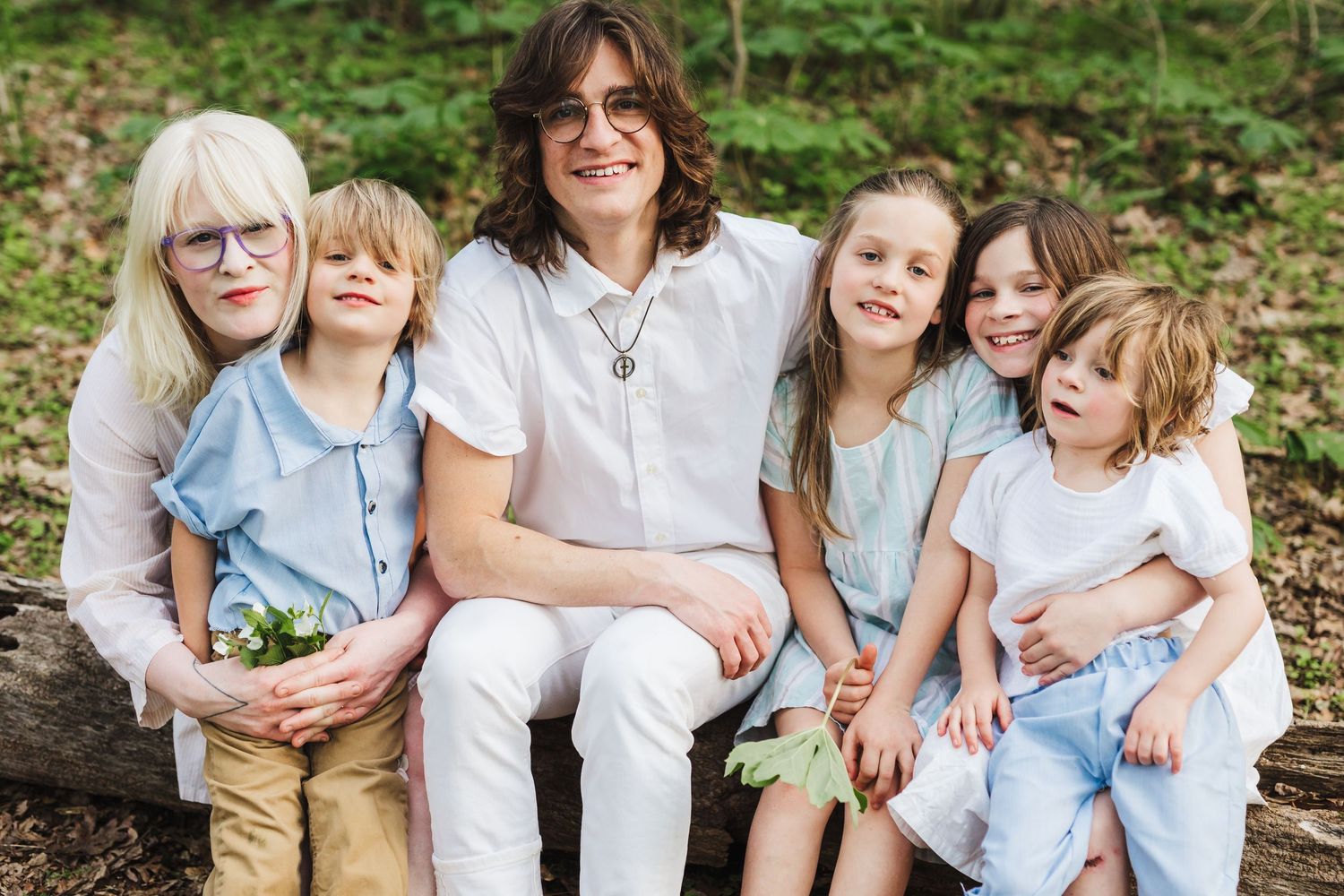 Family group sitting and laughing together outdoors in casual clothing against natural greenery background.