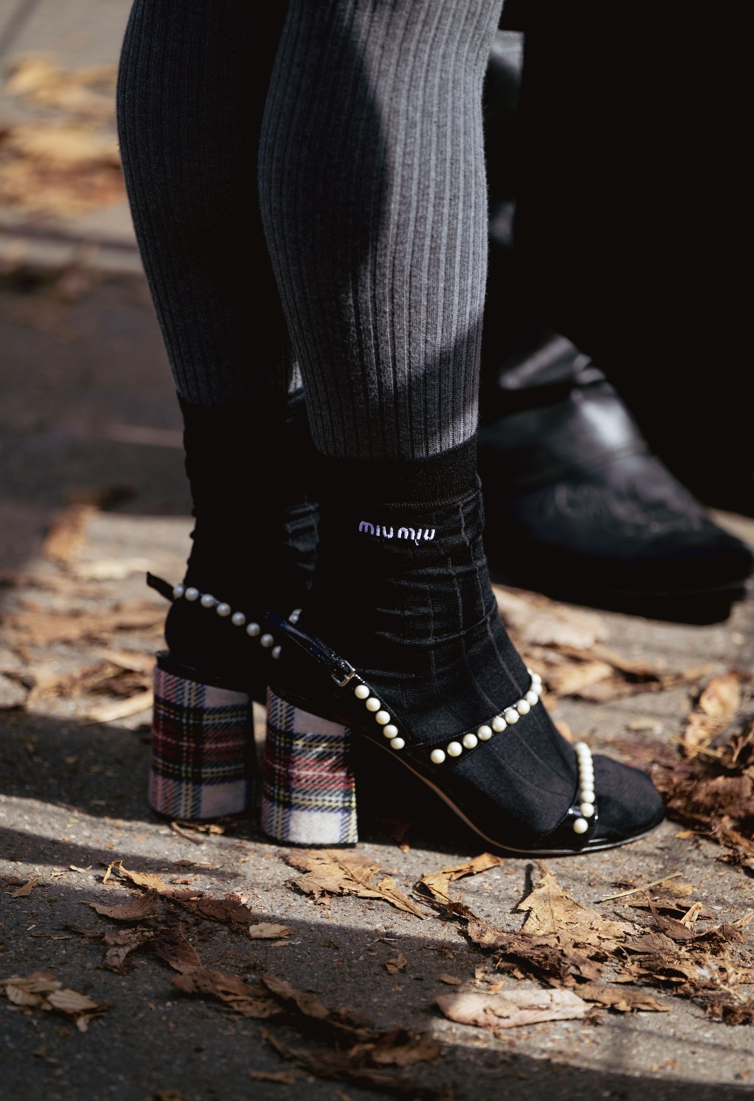 Black boots with pearl details and ribbed socks against fallen autumn leaves.