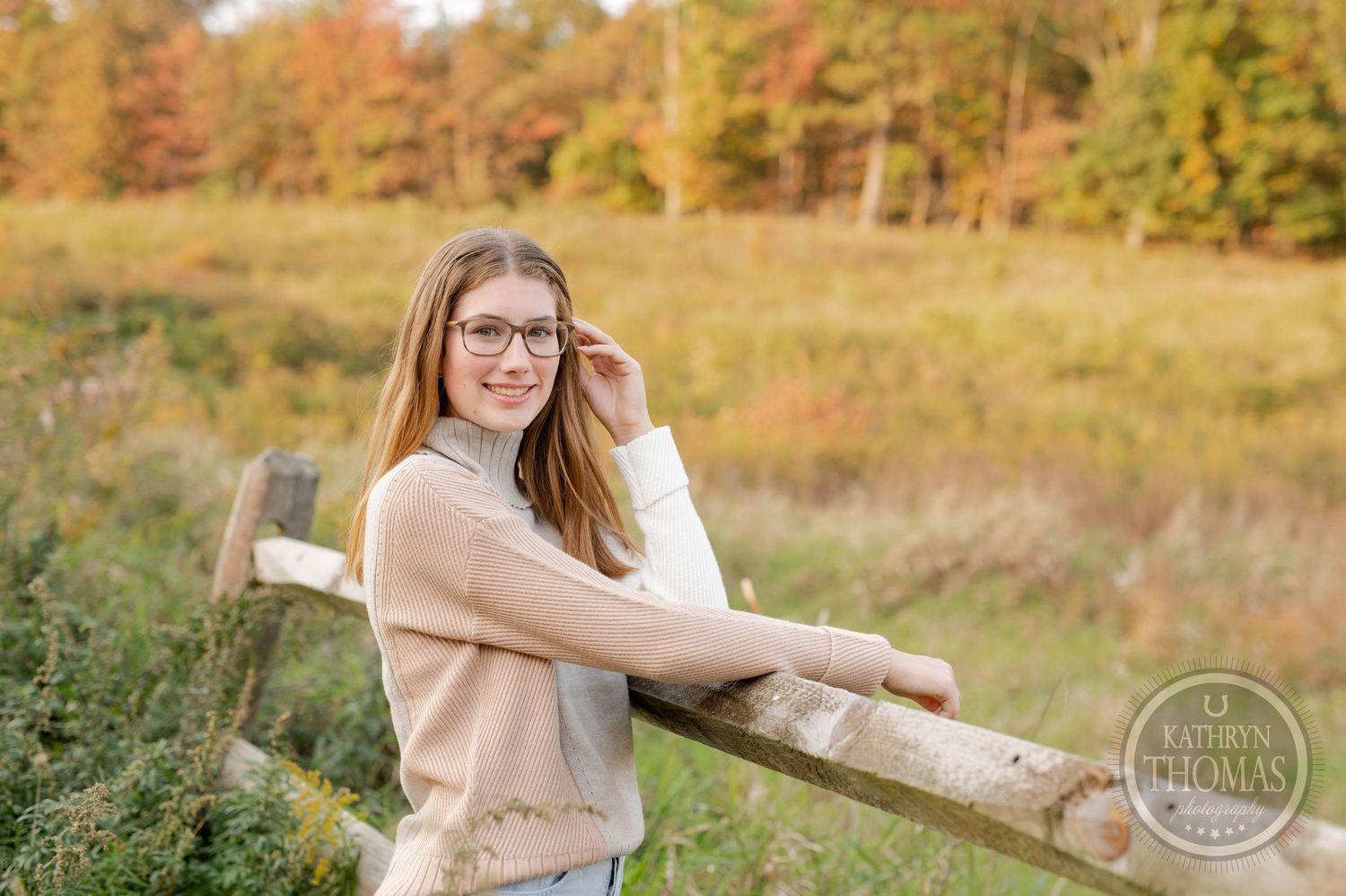 Casual outdoor portrait against wooden fence with fall foliage and warm evening light.