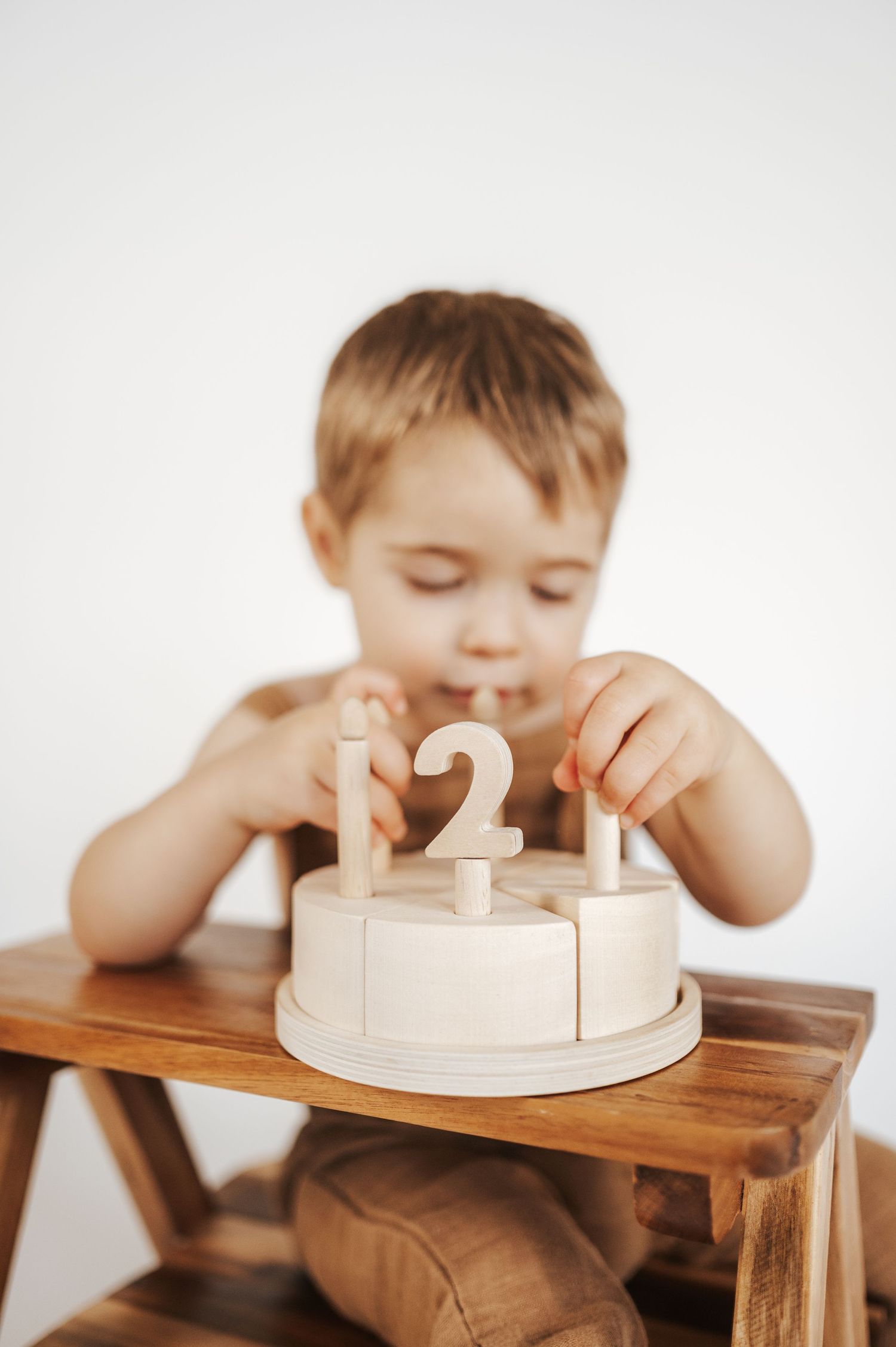Small child plays with wooden number blocks on a toy cake while sitting at a rustic wooden table.