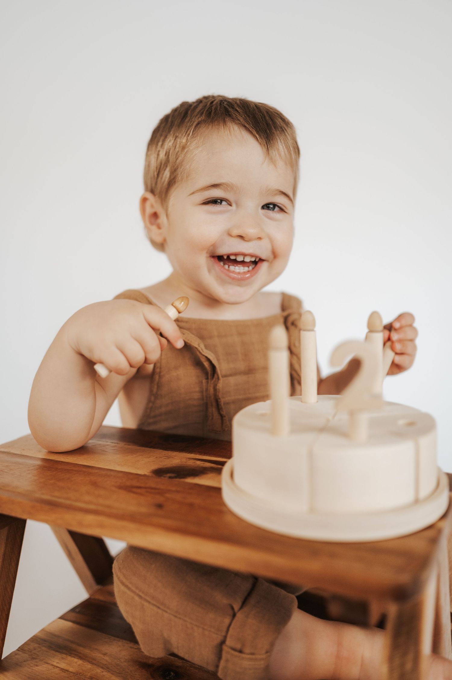 A happy child in earthtone clothing sits at a wooden table playing with a natural wood sensory toy or activity board.