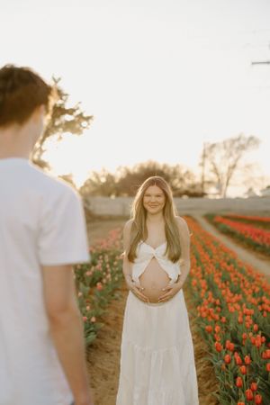 A couple shares a tender moment in a tulip field at sunset, with the woman in a flowing white dress showing her baby bump.