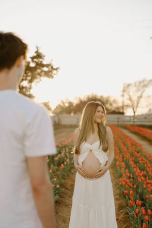 Couple poses together at sunset in a blooming orange tulip field on a tranquil rural farm.