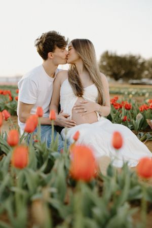 A romantic couple kisses in a field of blooming orange tulips during sunset, creating an intimate spring portrait.