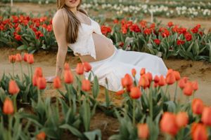 A maternity photo shoot in a vibrant orange tulip field featuring a white lace dress against the blooming spring flowers.