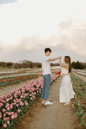 A romantic couple dances together on a path between rows of pink and red tulips at sunset.