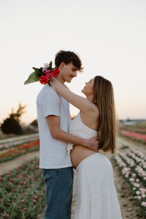 A tender moment between a couple in a flower field with red blooms at dusk.