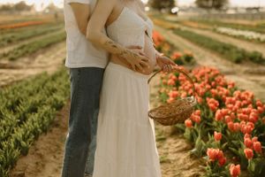 A couple embraces in a white dress at a tulip farm with rows of coral-colored tulips blooming in spring.