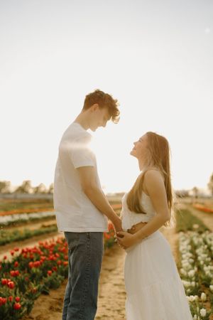 A couple shares an intimate moment in a flower field backlit by golden sunlight.