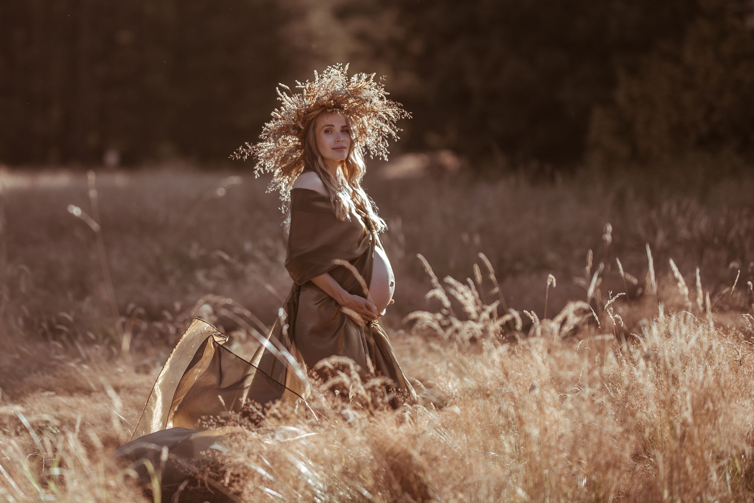 A silhouetted figure sits among tall grass in a sepia-toned field at sunset.