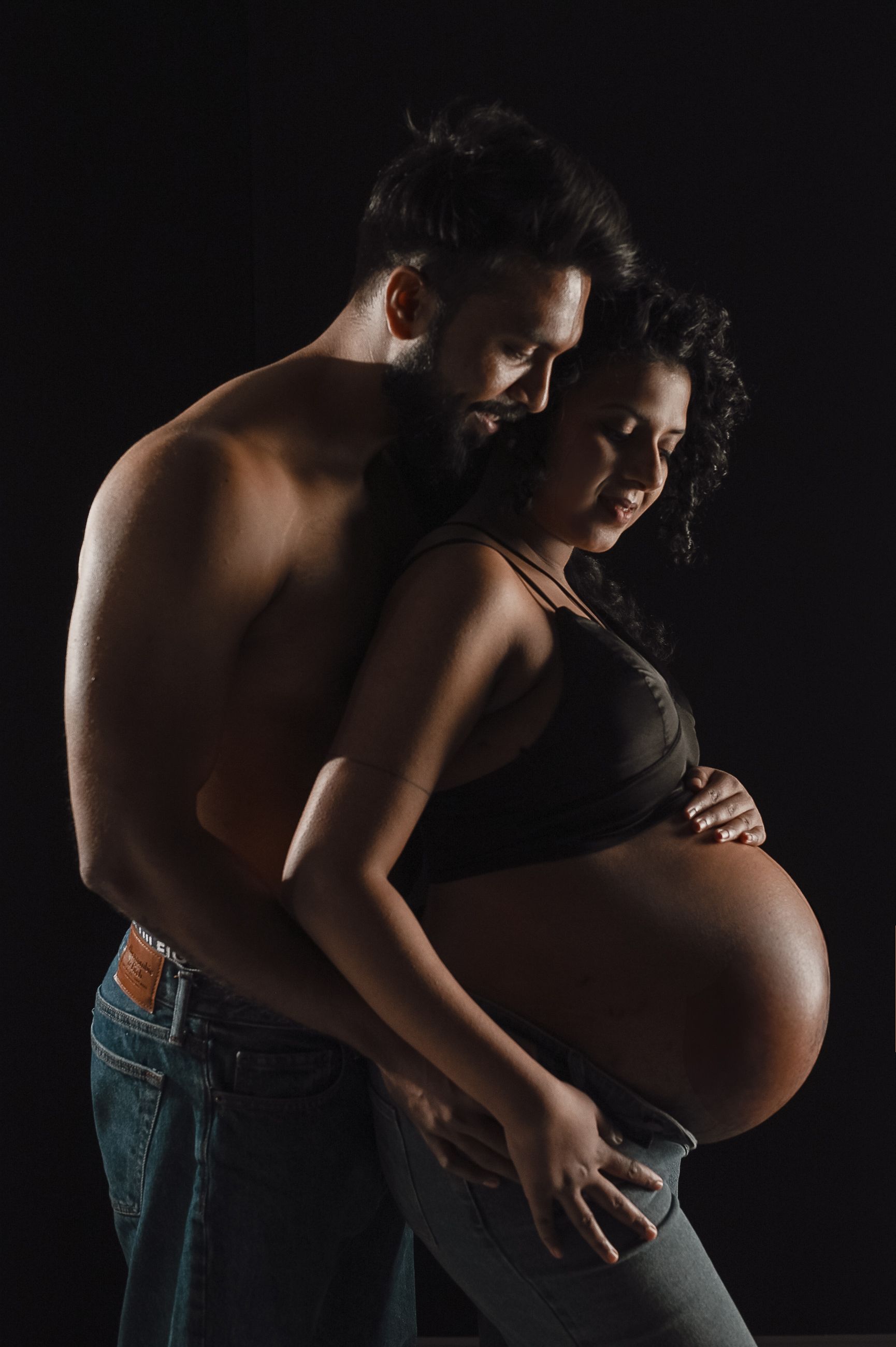 Dramatic silhouette maternity photo of couple embracing in dark setting.