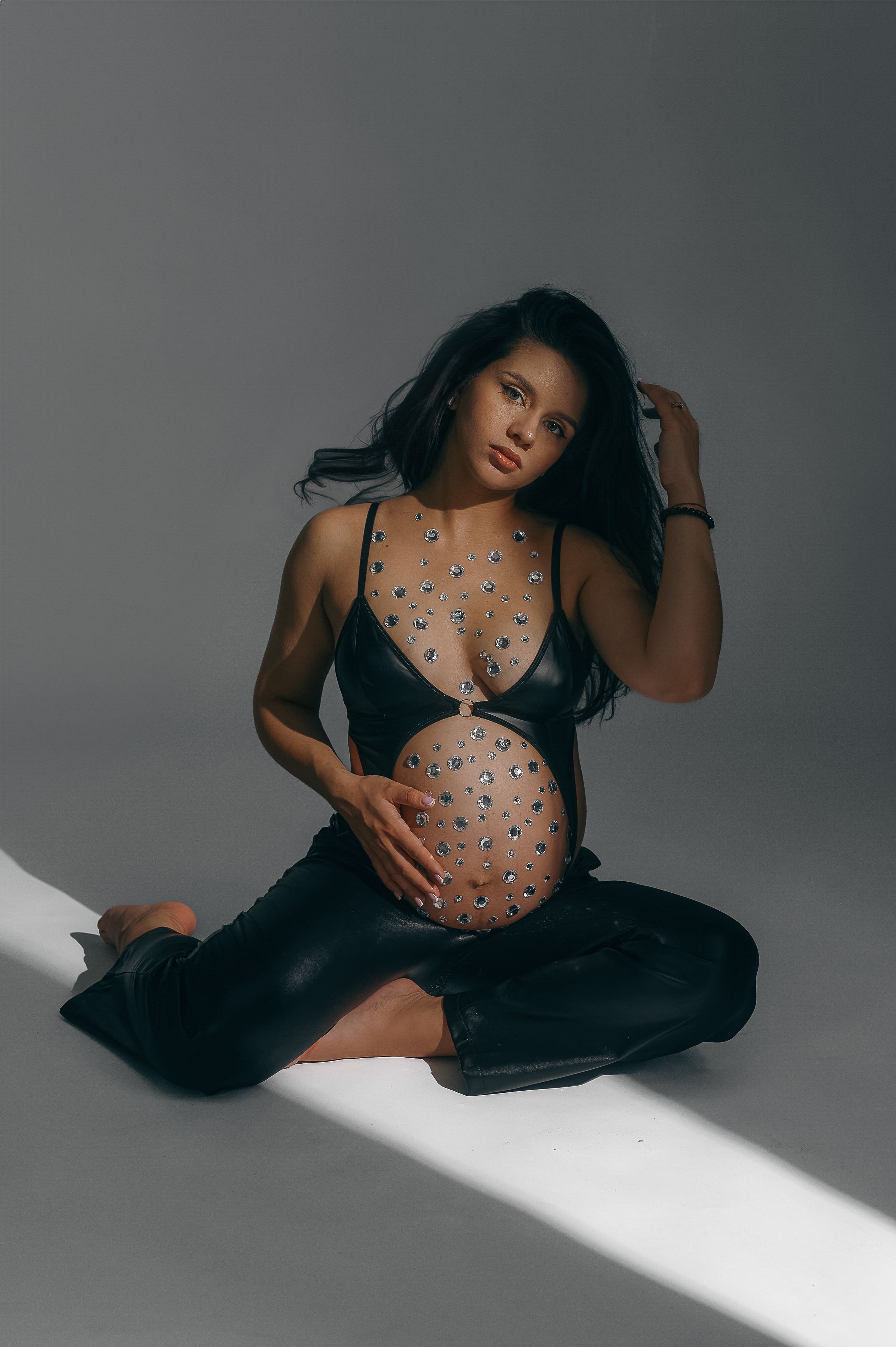 Studio maternity photo featuring a pregnant model in black attire with painted body art sitting in dramatic lighting.
