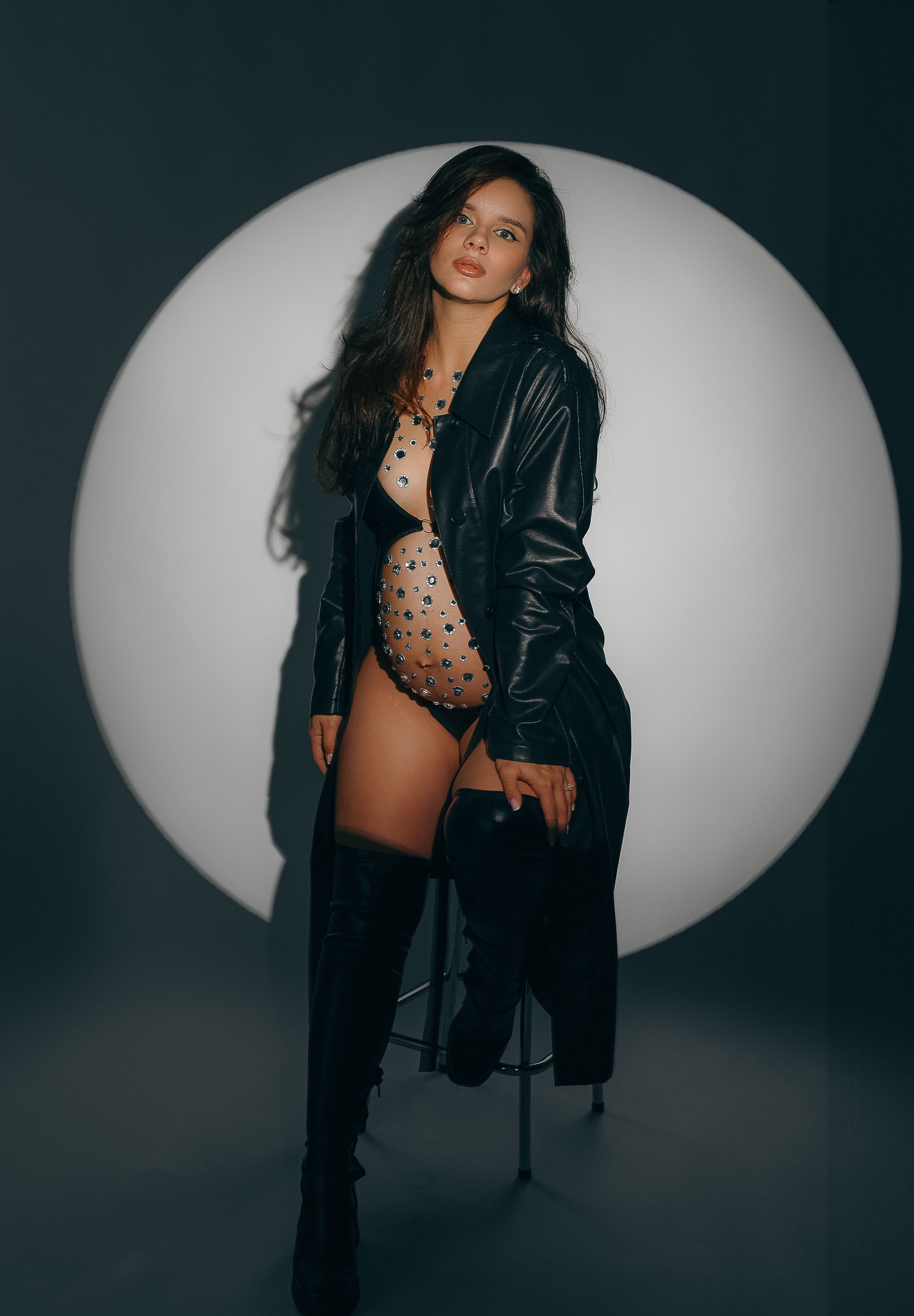 Fashion photoshoot against circular backdrop featuring a leather jacket and tall boots in moody lighting.