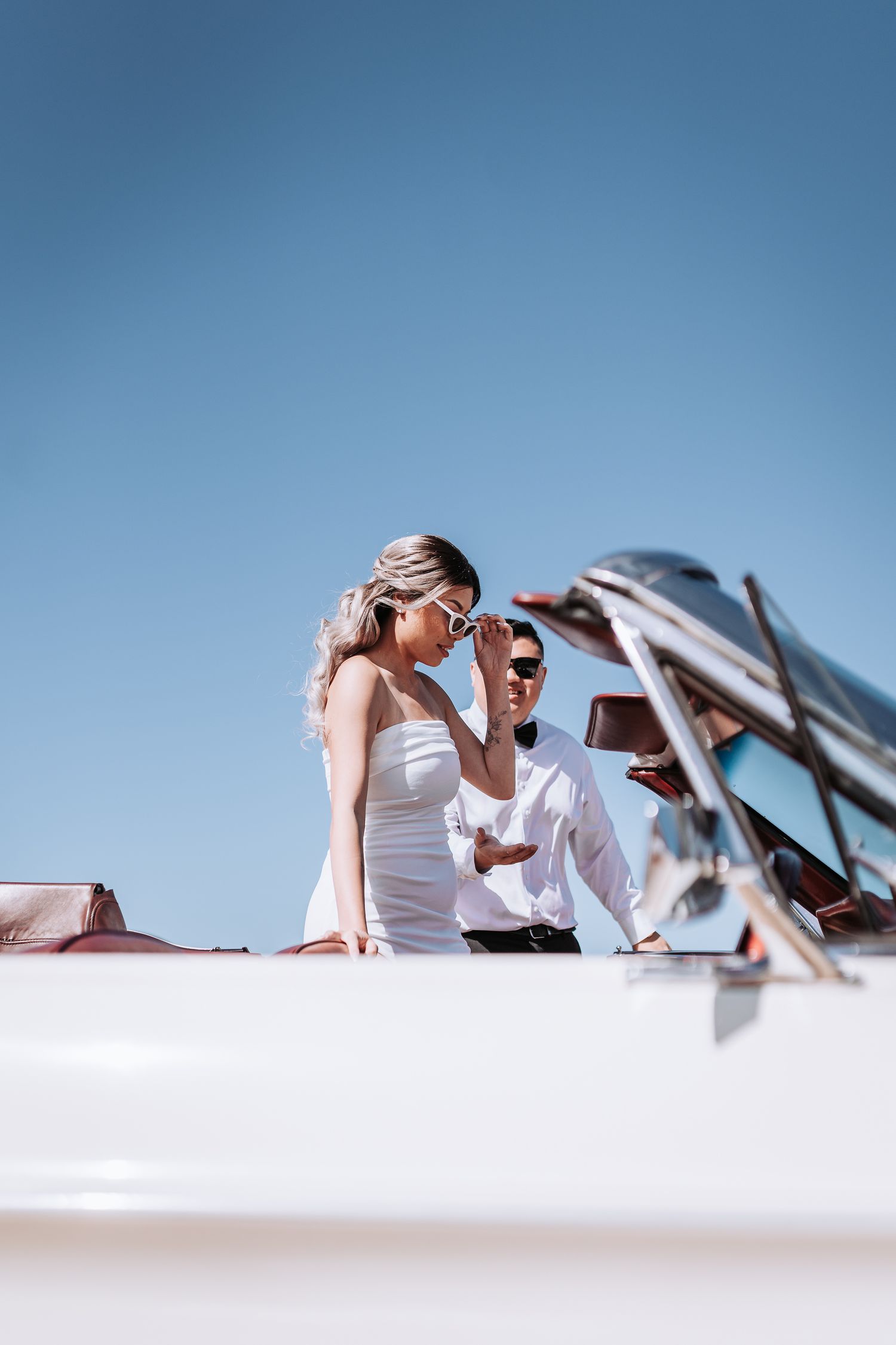 Couple in white summer attire aboard a boat against bright blue sky.