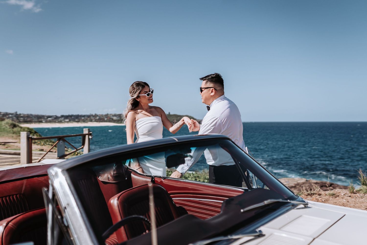 A classic white convertible car parked along a scenic coastal road with ocean views on a sunny day.