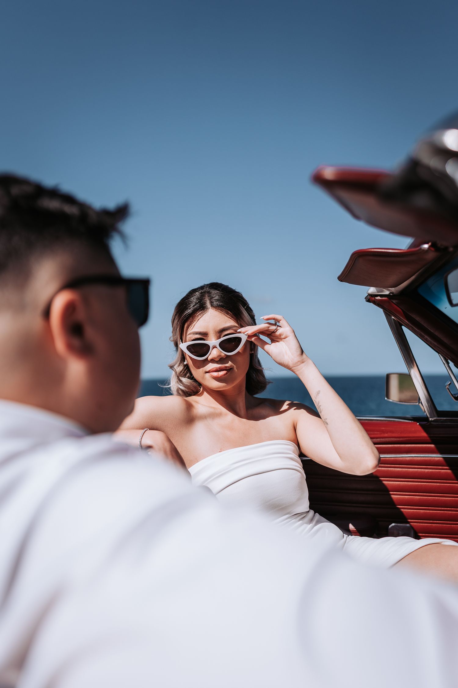 Fashionable couple in retro-styled photoshoot with classic convertible car by the ocean.