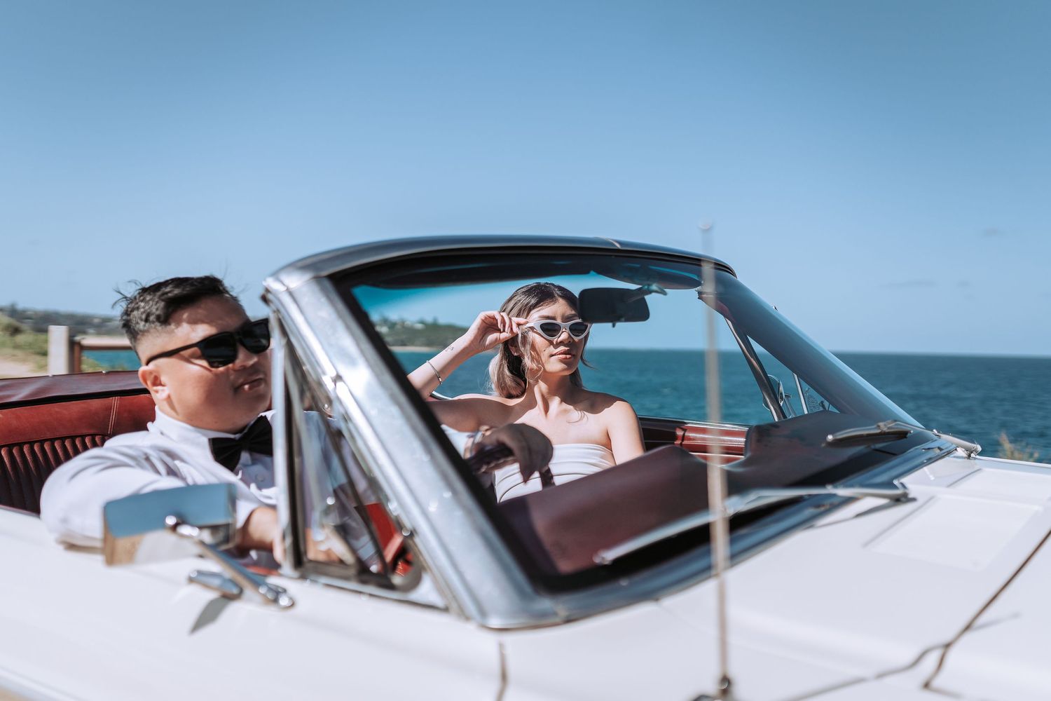 Couple in sunglasses enjoying a drive in classic white convertible by the seaside.