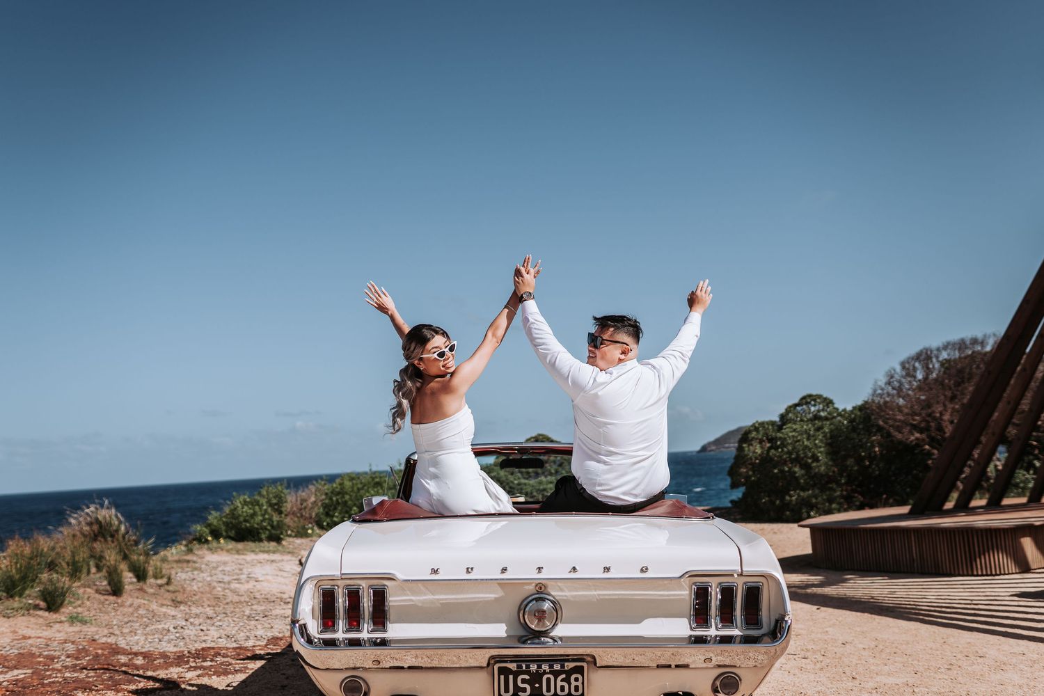 A joyful celebration on a vintage white Mustang convertible by the ocean.