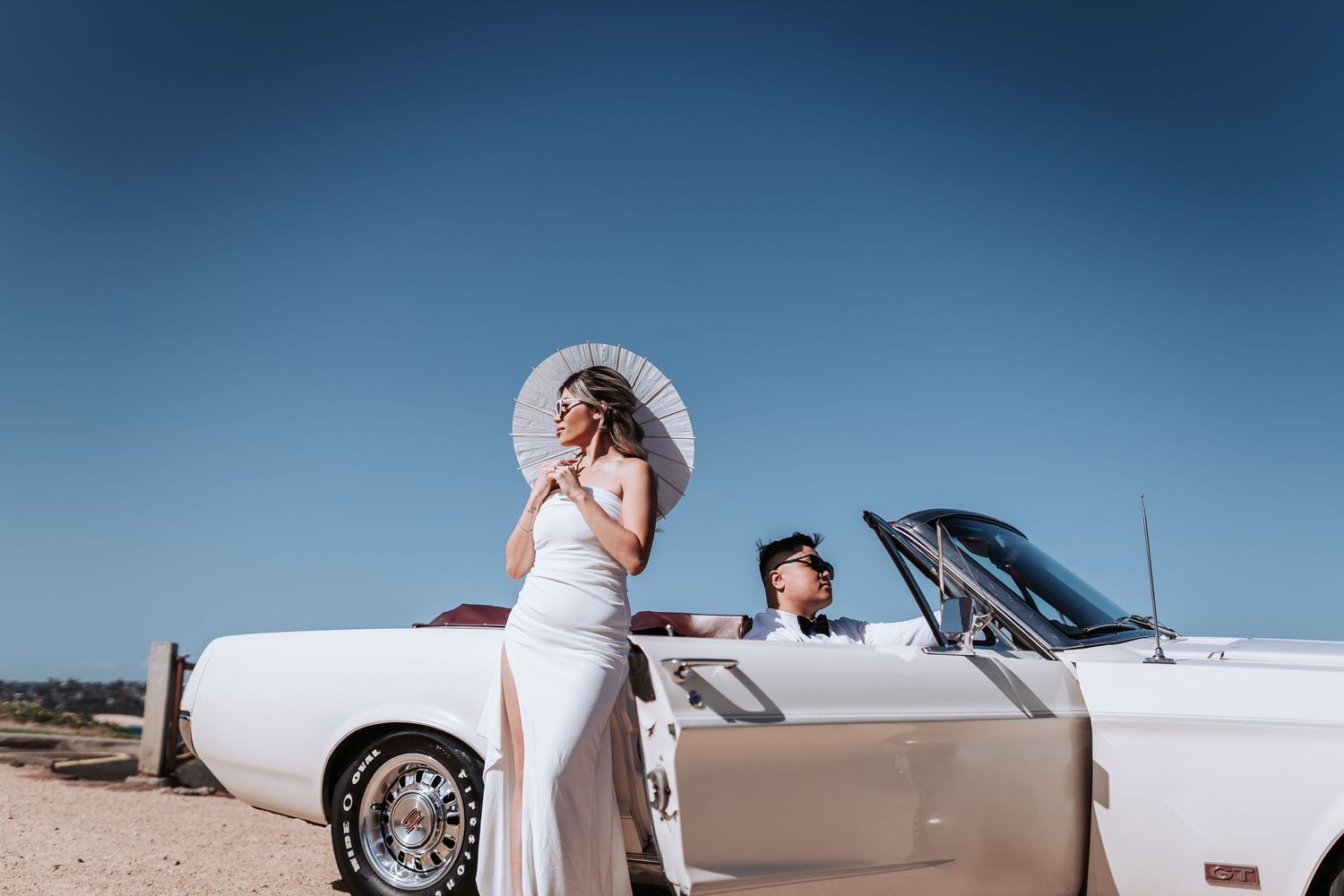 An elegant coastal photoshoot featuring a white parasol and vintage convertible.