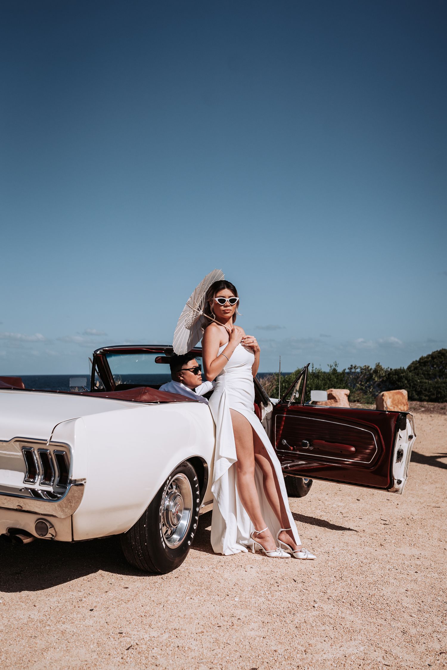 A glamorous photoshoot with a classic white Mustang convertible on a coastal road.